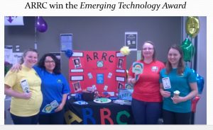 Four members of the team next to their booth containing information about product and promotional material