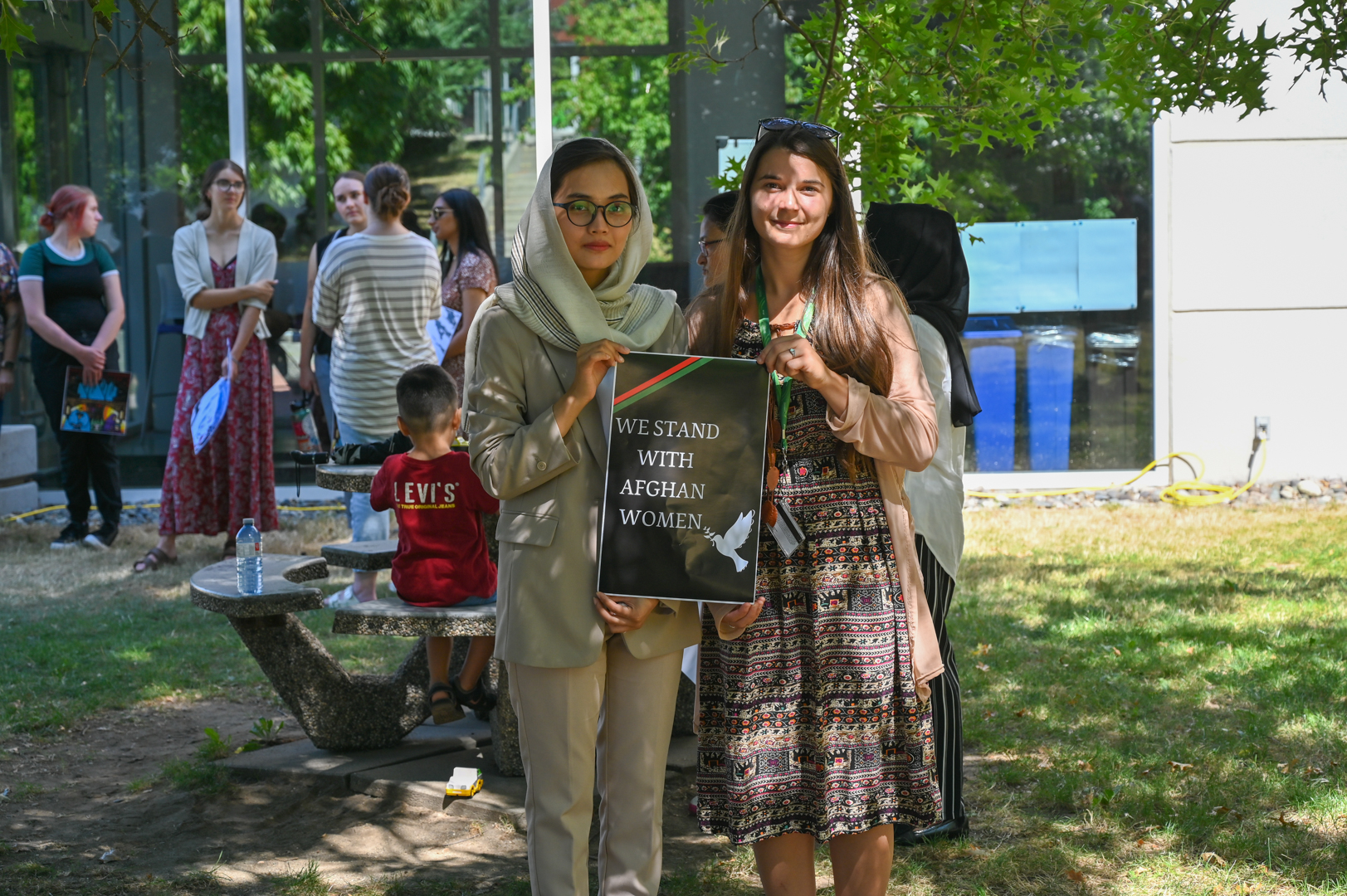 Photo of Sahar and CHASI Lead Researcher Chelsea Klassen standing beside each other, holding a sign that says "we stand with Afghan women" with an illustration of a white dove.