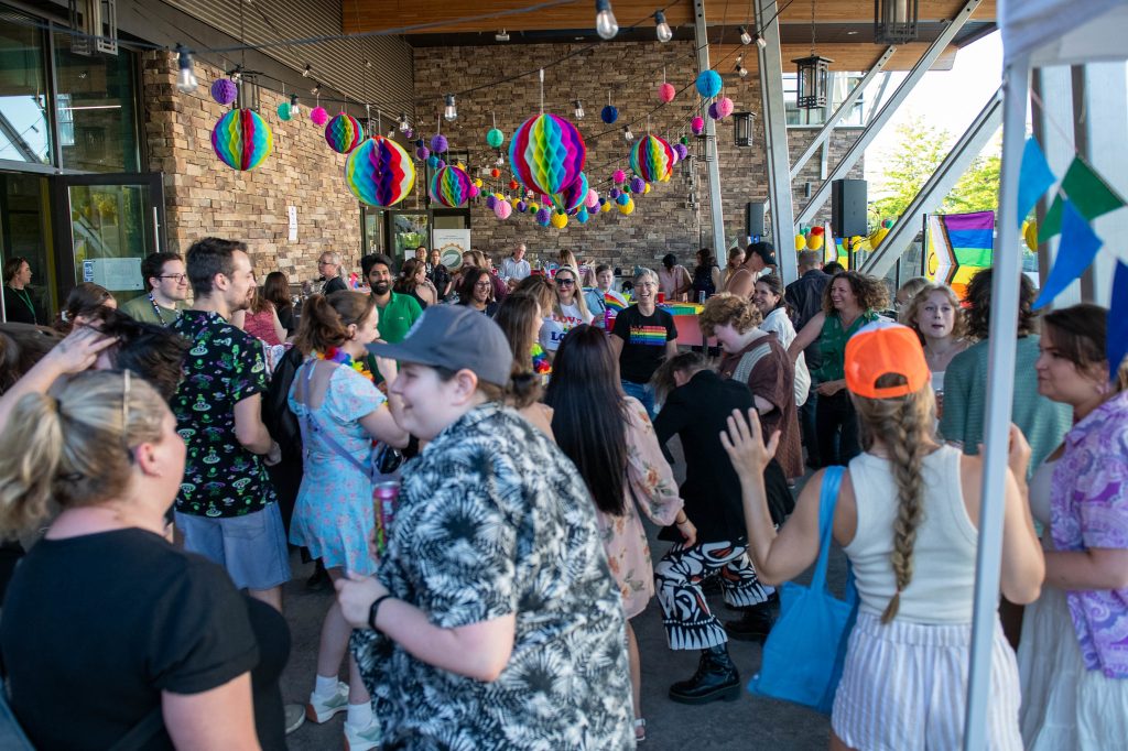 Photo of a packed patio full of people dancing with rainbow decorations all around them.