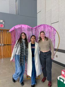 Three members of the CHASI team pose for a photo in front a a large heart-shaped decoration hung with purple tinsel.