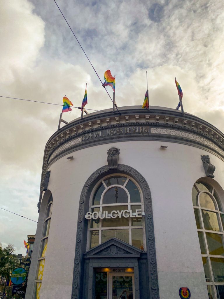 Photo of a building in the Castro District of San Diego. Five pride plags fly at the top, and beneath are the words "hope will never be silent."