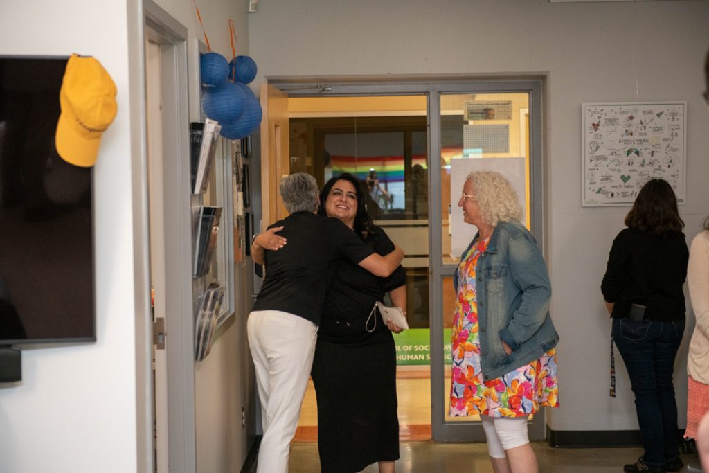 CHASI Director Dr. Martha Dow hugs a guest goodbye at the door to CHASI's office, while another guest stands by them. To the side, a guest looks at an art piece hanging on the wall, representing Changemaking work at UFV.