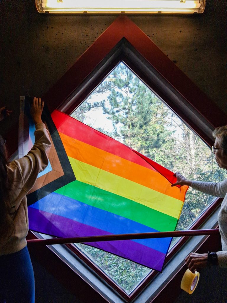 Photo of two people hanging a pride flag in a window at UFV