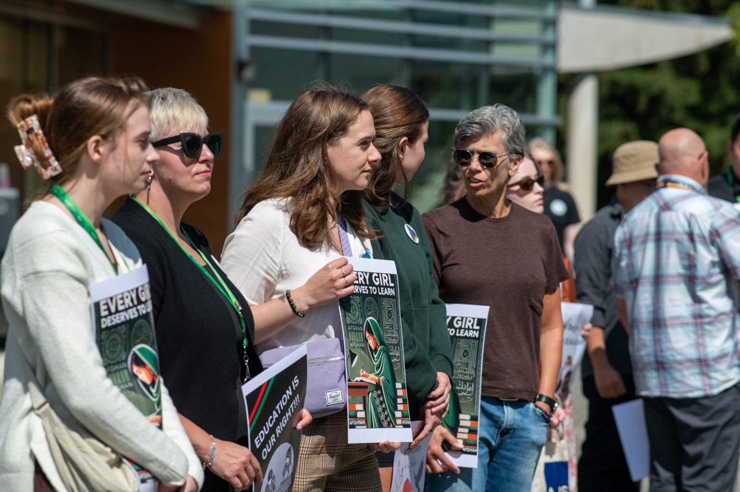 Photo of members of the CHASI team standing together together holding protest signs, talking to one another as they wait for the speeches to begin.