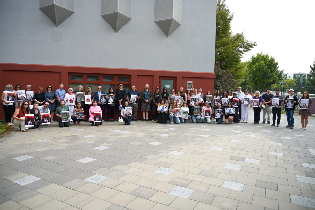 Photo of the gathered crowd of approximately 50 people standing in a line outdoors on UFV's Abbotsford campus. They are holding signs in support of women in Afghanistan.