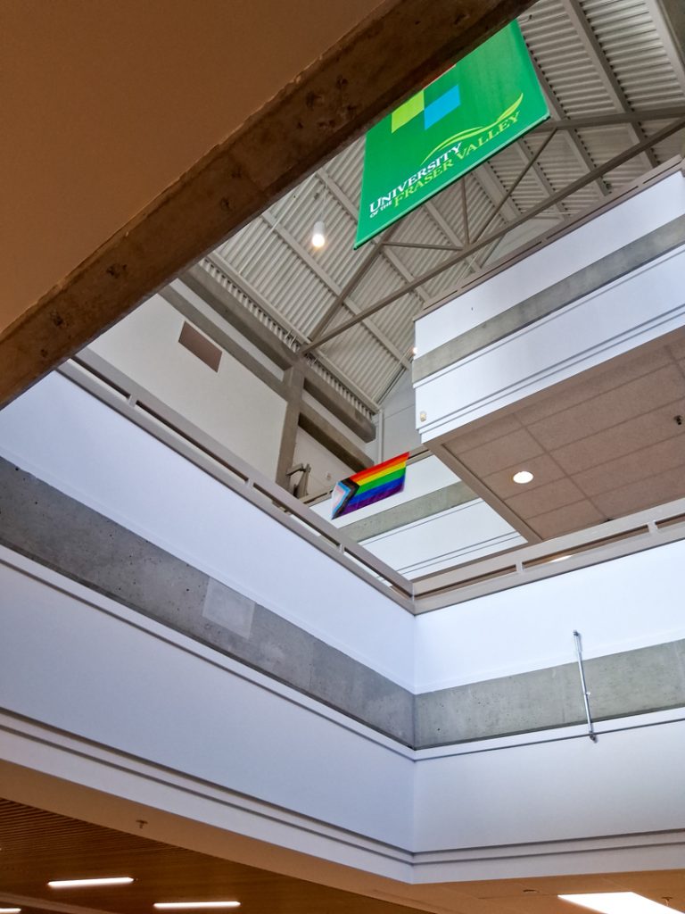 Photo looking up at a pride flag hanging from a balcony in UFV's great hall, viewed from two storeys down