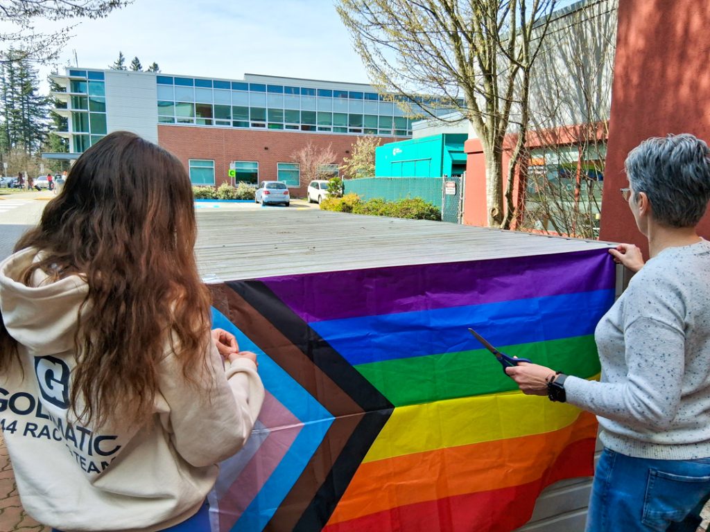 Photo of two people hanging a pride flag on a bike storage locker at UFV