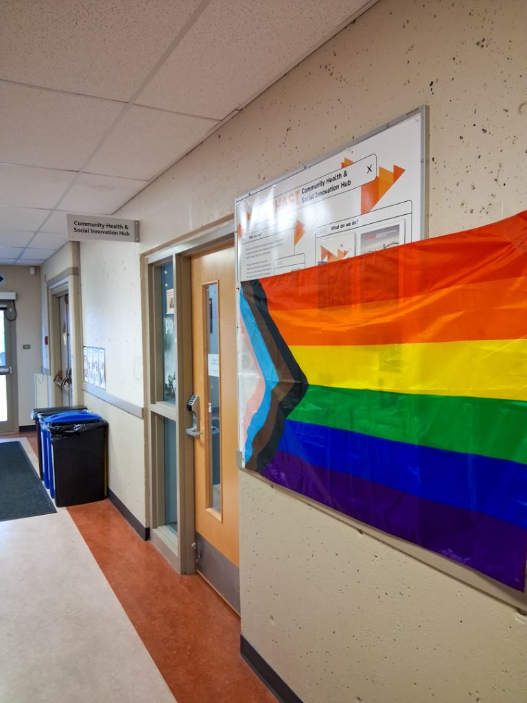 Photo of a trans flag hanging on the bulletin board outside CHASI's office door