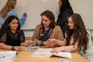 3 students looking at a science model and 2 students writing on a whiteboard