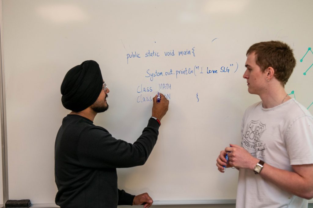 2 students writing computer code on the white board. 