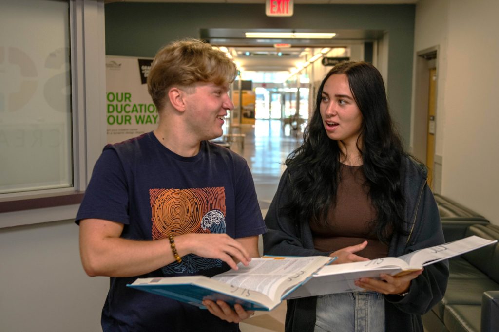 2 students with open textbooks in mid-conversation.