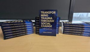 Display of "Transforming Trauma Through Social Change" books stacked nicely