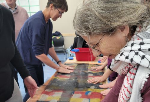 Woman looking down at a table with cloth on it. Multiple hands are also on the cloth