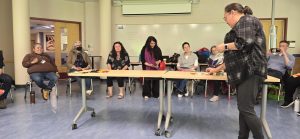 a woman standing up while many people are sitting behind a table