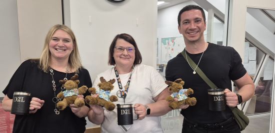 3 staff members holding D2L merch and smiling at the camers