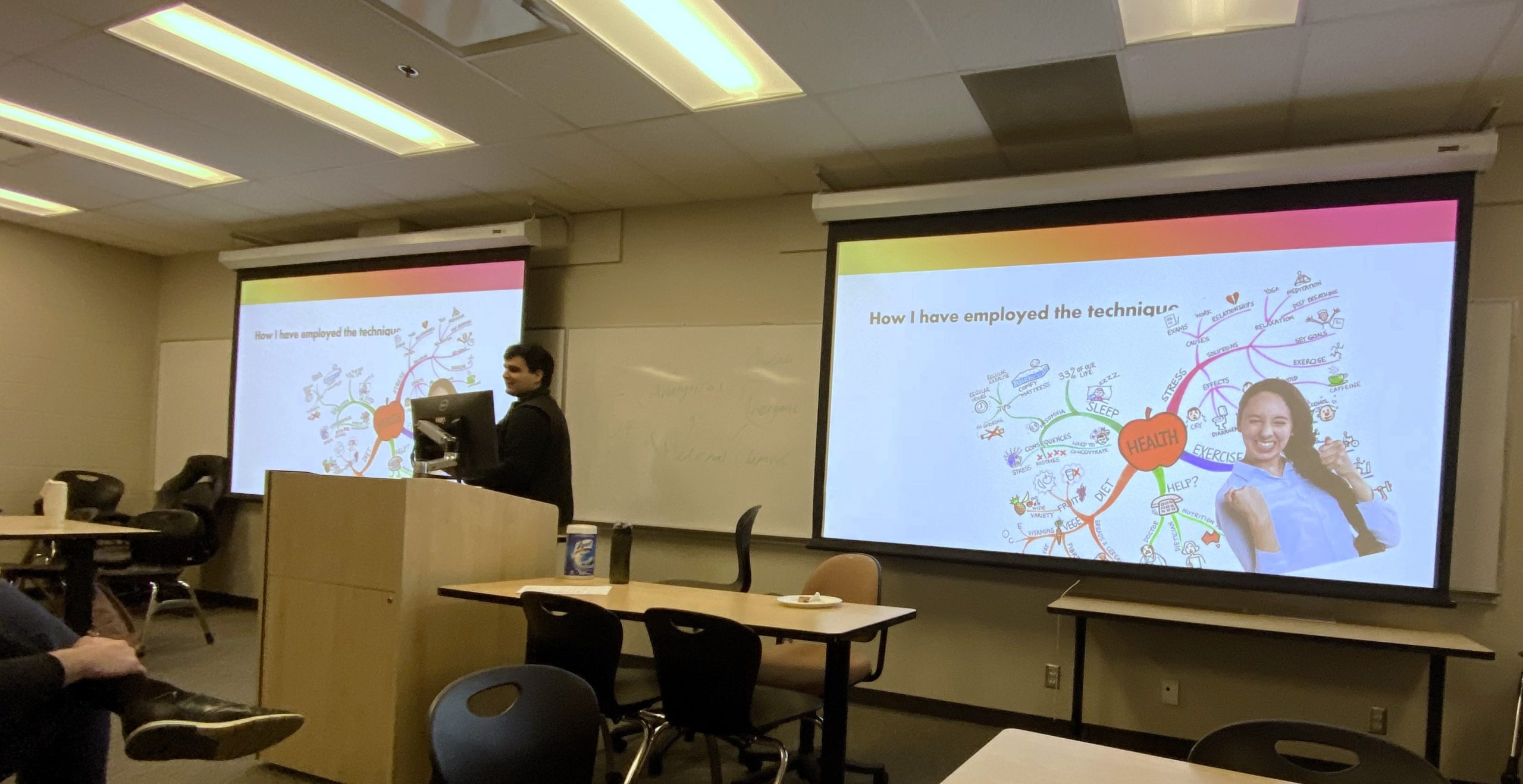 Arthuri at the front of the class in the middle of 2 projector screens