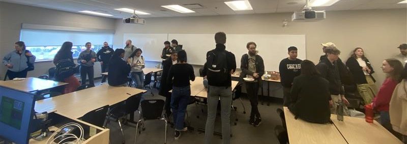 a busy classroom where all the students are standing up conversing with eachother