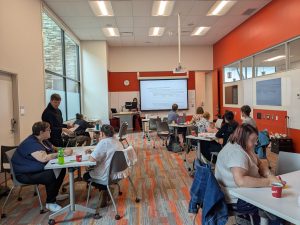 The TLC team in a meeting room in K building seated and facing the projector