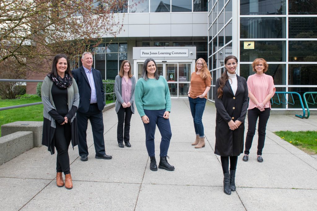 The University of the Fraser Valley (UFV) Research and Graduate Studies Office Staff standing in front of the Peter Jones Learning Commons on UFV's Abbotsford Campus